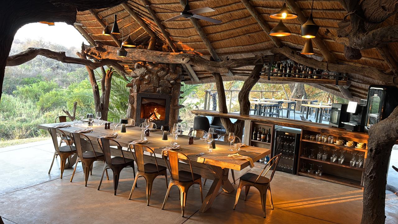 Custom lodge dining table under a thatched lapa, built by Crafter Mo