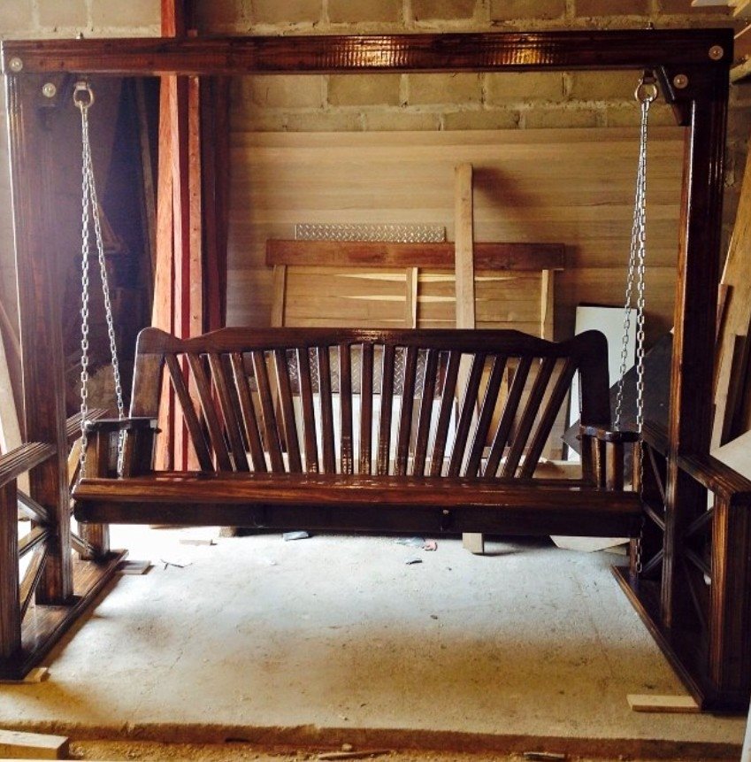 Dark stained wooden porch swing with slat back on a timber stand